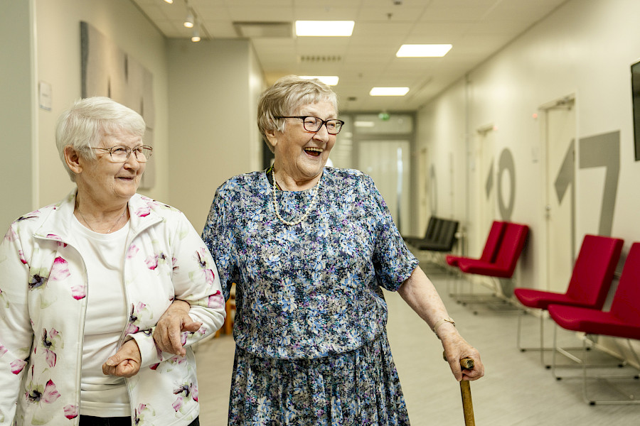 Kuvassa kaksi senioria kävelee Pk Terveyden vastaanottotiloissa. Geriatrian eli ikäihmisen vastaanotolla edetään tarvittessa rauhallisempaan tahtiin ja selvitetään useampi mieltä painava oire tai asia läpi.